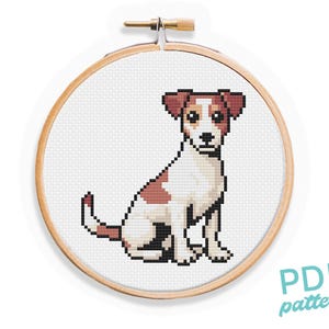Può includere: Schema di punto croce di un Jack Russell Terrier marrone e bianco seduto su uno sfondo bianco. Il motivo è in un telaio da ricamo in legno.