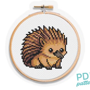 May include: A cross-stitch pattern of a hedgehog in a wooden embroidery hoop. The hedgehog is brown and tan with a pixelated design. The text "PDF pattern" is in the lower right corner.