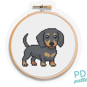 May include: Cross-stitch pattern of a dachshund dog in a wooden embroidery hoop. The dog is depicted in a pixelated style with black, tan, and brown colors. The text "PDF pattern" is visible in the lower right corner.