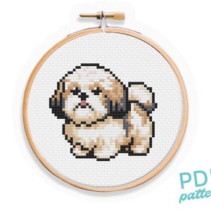Op de afbeelding: Kruissteekpatroon van een Shih Tzu hond in een houten borduurring. De hond is bruin en wit met zwarte oren en een zwarte neus. Het patroon is op witte Aida-stof.