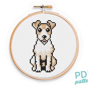 May include: Cross stitch pattern of a brown and white dog sitting with its tongue sticking out. The pattern is in a wooden embroidery hoop.