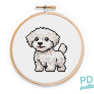 May include: Cross stitch pattern of a white dog in a wooden embroidery hoop. The dog is a small breed with fluffy white fur and black eyes. The pattern is in PDF format.