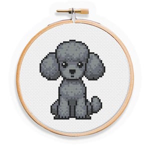 Può includere: Un telaio da ricamo a punto croce con un disegno di barboncino grigio. Il cane è raffigurato in uno stile pixelato, con una testa e una coda soffici. Il ricamo è ambientato su uno sfondo bianco, incorniciato da un telaio di legno.