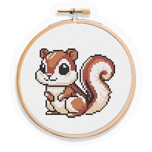 May include: A cross-stitch embroidery of a cartoon squirrel in a wooden hoop. The squirrel is brown, white, and beige with black outlines. The embroidery is on white fabric, and the hoop is made of light-colored wood.