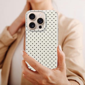 May include: A smartphone case featuring a cream-colored background with a repeating pattern of small black polka dots. The case has a clear border around the edges and a cutout section for the triple-lens camera system on the back of the device.