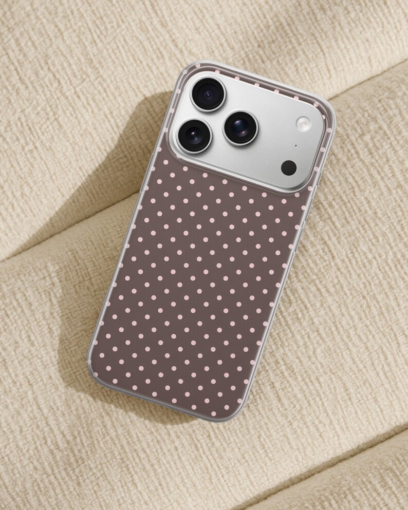 May include: A smartphone case featuring a dark brown background with a repeating pattern of small, light pink polka dots. The case is transparent around the edges and includes a rectangular cutout for the camera lenses and flash module.
