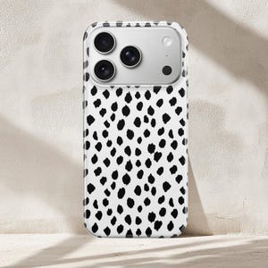 May include: A smartphone case featuring a white background with a repeating pattern of irregular black spots. The case has a clear border and a rectangular cutout at the top for the camera lenses, which are visible as three circular black circles.