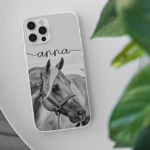 May include: Clear phone case featuring a black and white image of a horse's head with a bridle. The name "anna" is written in cursive script above the horse image. The case has a clear border and a camera cutout.
