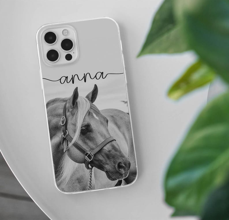 May include: Clear phone case featuring a black and white image of a horse's head with a bridle. The name "anna" is written in cursive script above the horse image. The case has a clear border and a camera cutout.