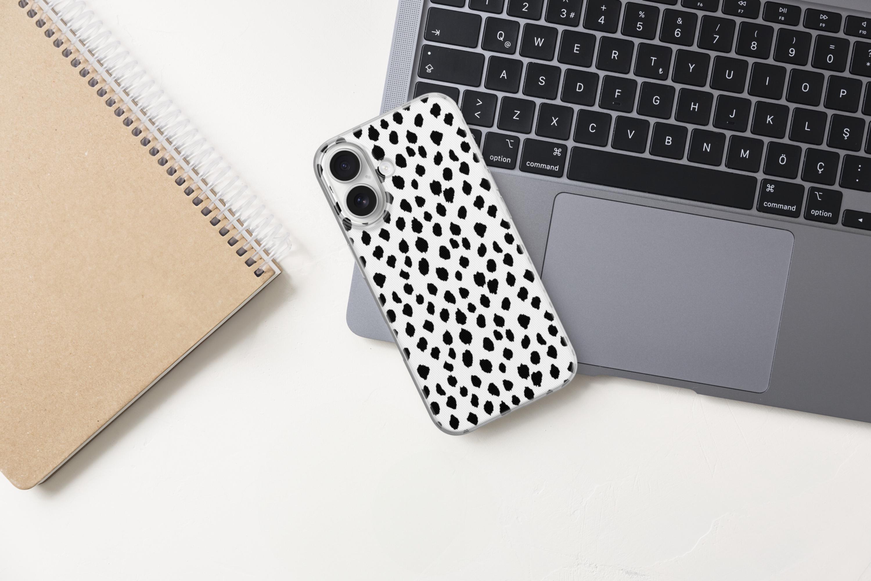 May include: A smartphone case featuring a white background with a repeating pattern of irregular black spots. The case has two circular cutouts for camera lenses on the upper left side and is positioned on a dark gray laptop keyboard.