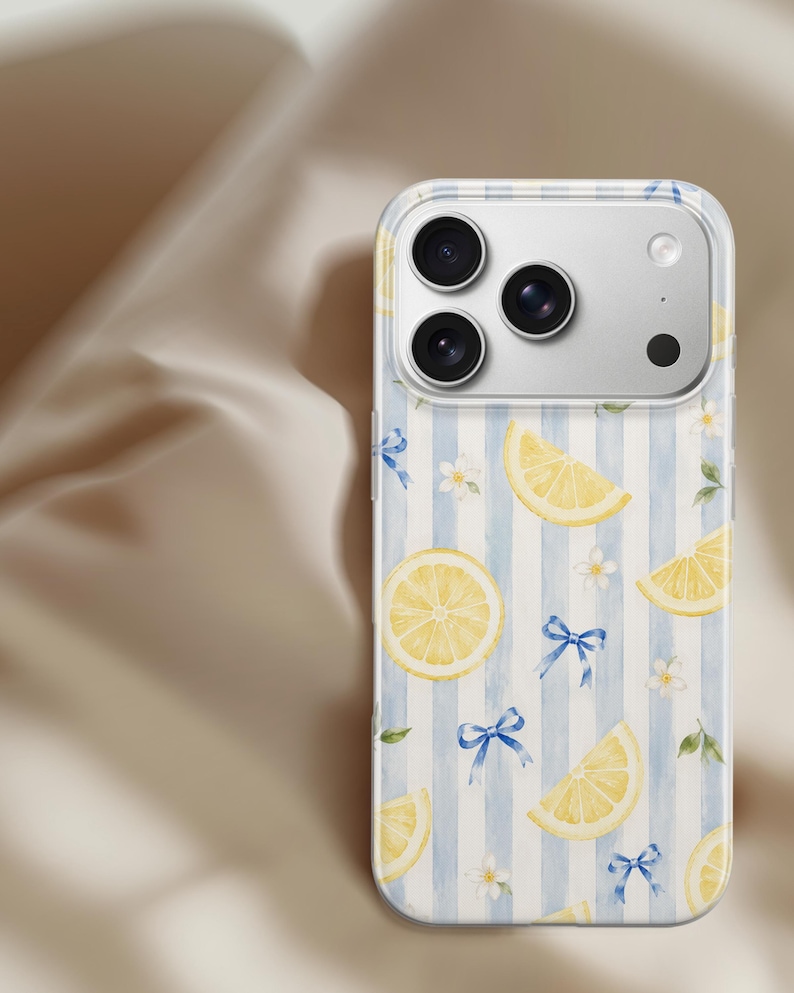 K&ouml;nnte beinhalten: Eine transparente Smartphone-H&uuml;lle mit einem Muster aus gelben Zitronenscheiben, kleinen wei&szlig;en Bl&uuml;ten und blauen Schleifen auf einem Hintergrund mit vertikalen hellblauen und wei&szlig;en Streifen. Die H&uuml;lle hat eine Aussparung f&uuml;r eine Dreifachkamera.