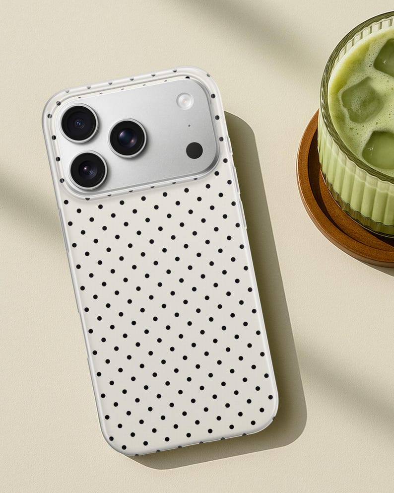 May include: A smartphone case featuring a white background with a repeating pattern of small black polka dots. The case has a clear border and a rectangular cutout at the top left corner to accommodate a triple-lens camera system and a flash.