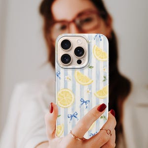 K&ouml;nnte beinhalten: Eine Smartphone-H&uuml;lle mit einem hellblau-wei&szlig; gestreiften Muster, das mit gelben Zitronenscheiben, kleinen wei&szlig;en Bl&uuml;ten und zarten blauen Schleifen verziert ist, die &uuml;ber die Oberfl&auml;che verteilt sind, inklusive Aussparung f&uuml;r die Kameralinse.