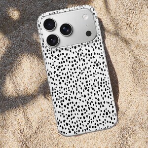 May include: A smartphone case featuring a white background with a dense pattern of irregular black spots. The case has a clear border and a rectangular cutout at the top left corner to accommodate a triple-lens camera system and a flash.