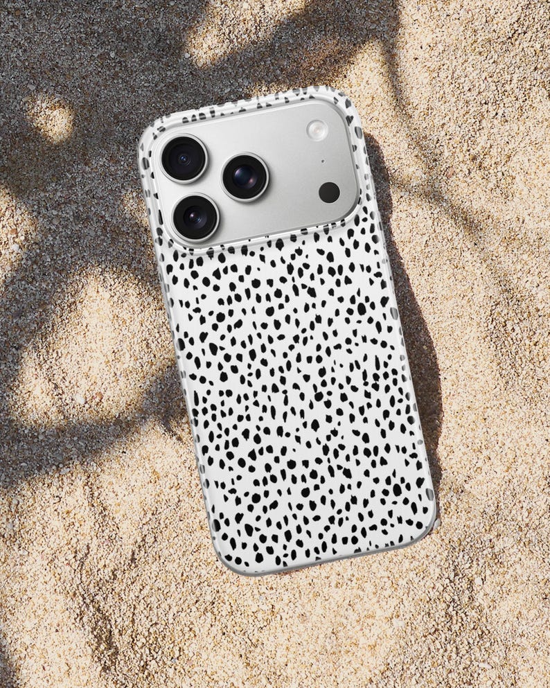 May include: A smartphone case featuring a white background with a dense pattern of irregular black spots. The case has a clear border and a rectangular cutout at the top left corner to accommodate a triple-lens camera system and a flash.
