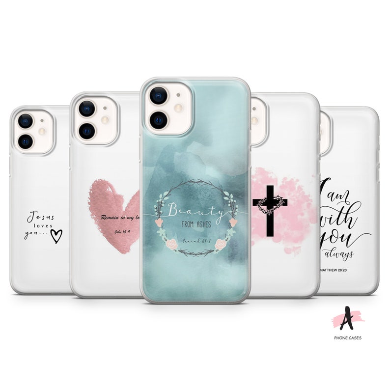 May include: Set of four clear phone cases with different designs. The first case features a pink heart with the text "Jesus loves you...♡" and "Remain in my love John 15:9". The second case features a watercolor background with a floral wreath and the text "Beauty from ashes Isaiah 61:3". The third case features a pink watercolor background with a black cross and a heart. The fourth case features a pink watercolor background with the text "I am with you always Matthew 28:20".