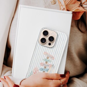 K&ouml;nnte beinhalten: Eine transparente Smartphone-H&uuml;lle mit hellblau-wei&szlig;em vertikalem Streifenmuster und einer Grafik eines Holzschildes mit der Aufschrift Sunshine, Relax, Ocean und Beach, erg&auml;nzt durch ein Surfbrett und korallenfarbenes Blattwerk.