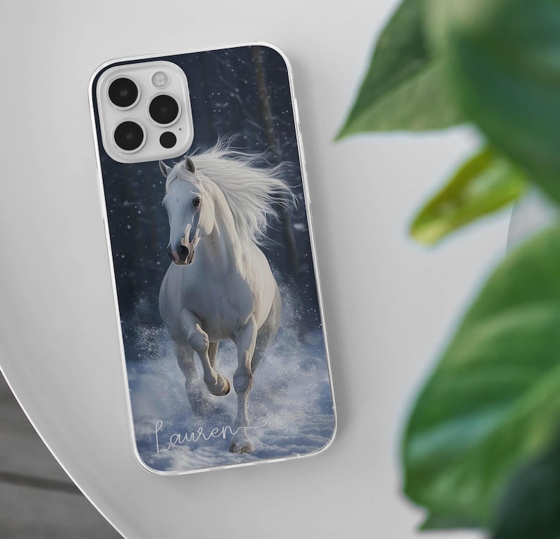 May include: A phone case featuring a white horse running through snow. The image has a winter theme with a dark background. The name "Lauren" is written in cursive at the bottom of the case.