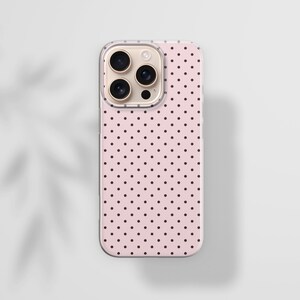May include: A smartphone case featuring a light pink background with a repeating pattern of small black polka dots. The case has a rectangular shape with rounded corners and a cutout section at the top left for a triple camera lens system.