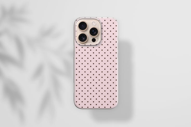 May include: A smartphone case featuring a light pink background with a repeating pattern of small black polka dots. The case has a rectangular shape with rounded corners and a cutout section at the top left for a triple camera lens system.