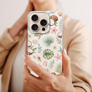 K&ouml;nnte beinhalten: Eine transparente Smartphone-H&uuml;lle mit einem wiederkehrenden Muster aus tropischen Elementen, darunter gr&uuml;ne Palmenbl&auml;tter, Monstera-Bl&auml;tter, braune Kokosn&uuml;sse, rosa Seesterne, Muscheln und kleine Blumen auf wei&szlig;em Hintergrund.