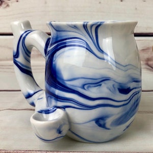 May include: White ceramic mug with a blue marbled design. The mug has a handle and a small spout on the side.