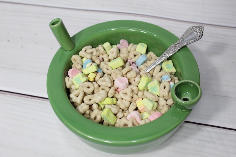 K&ouml;nnte beinhalten: Eine gr&uuml;ne Keramiksch&uuml;ssel mit einem Ausguss auf jeder Seite, gef&uuml;llt mit einem Fr&uuml;hst&uuml;cksm&uuml;sli mit Marshmallows. Ein silberner L&ouml;ffel befindet sich in der Sch&uuml;ssel.