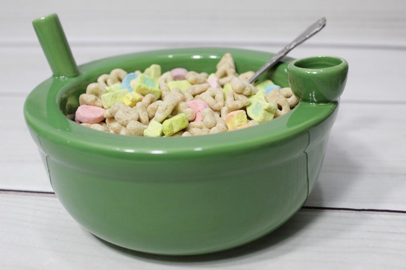 K&ouml;nnte beinhalten: Eine gr&uuml;ne Keramiksch&uuml;ssel mit einem Ausguss und einem Griff, gef&uuml;llt mit Fr&uuml;hst&uuml;cksflocken mit Marshmallows.