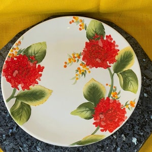 May include: White ceramic dinner plate with a floral design. The plate features red flowers with green leaves and yellow accents.