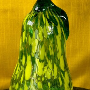 Könnte beinhalten: Eine grüne Glasbirne mit gelber Marmorierung. Die Birne ist ein dekoratives Objekt mit einem einzigartigen, mundgeblasenen Design.