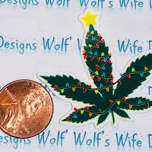 May include: A green marijuana leaf with a yellow star on top, decorated with colorful Christmas lights. The leaf is a Christmas tree.