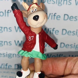 Könnte beinhalten: Eine rot-weiße Rentierfigur mit Schlittschuhen. Das Rentier trägt eine rote Jacke mit einer weißen Nummer 87 auf der Vorderseite. Das Rentier hält seinen rechten Arm in die Luft.