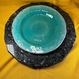 May include: A turquoise blue ceramic dinner plate with a distressed finish sits on top of a black octagonal charger plate.