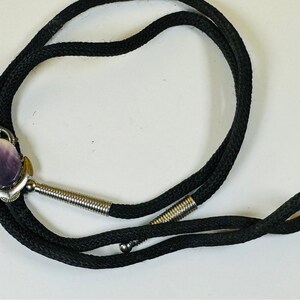 May include: A black bolo tie with a silver anchor pendant featuring a purple shell cameo.