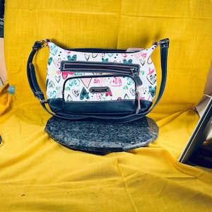 Stone & Co. sac à bandoulière imprimé coeur et étoiles de couleur blanche avec une bordure bleu très foncé plusieurs poches la plupart des poches pour cartes zippées similicuir