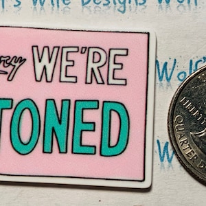 May include: A pink and white sticker with the text "Sorry WE'RE STONED" in teal and white lettering.