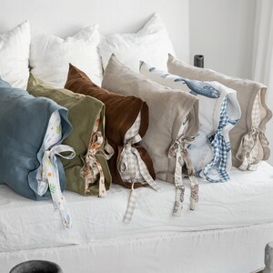 May include: A collection of linen pillowcases in various colors, including blue, green, and brown, with patterned ties. Some pillowcases feature printed designs, such as a whale. The pillows are arranged on a white bed, creating a cozy and inviting atmosphere.