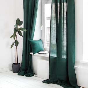 May include: A pair of dark green linen curtains hang in a window with a white windowsill and a white radiator underneath. A small green cushion sits on the windowsill.