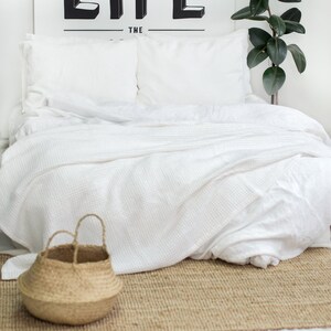 Può includere: Letto bianco con biancheria da letto bianca e un cesto intrecciato su un tappeto marrone. La parete dietro il letto ha il testo "ULTIMATE QUESTION OF LIFE THE" scritto in nero.