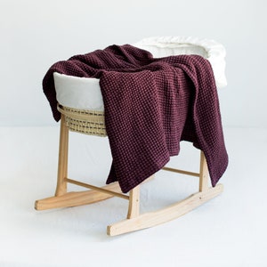 Puede incluir: Un moisés de madera con base de balanceo, forro blanco y una manta de tejido tipo waffle color burdeos en su interior.