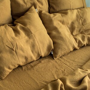 Puede incluir: Primer plano de una cama con un edred&oacute;n de lino marr&oacute;n y varias almohadas de lino marr&oacute;n. La ropa de cama est&aacute; arrugada y tiene un aspecto natural y texturizado.