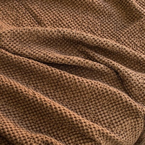 May include: A close-up of a brown textured fabric with a waffle-like pattern. The fabric is soft and has a subtle sheen.