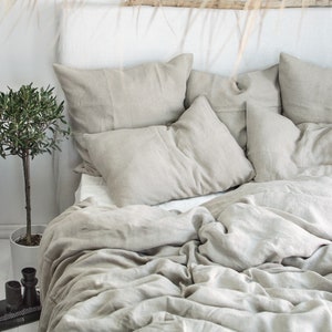 May include: A bed with a white headboard and a linen duvet cover and pillows in a light beige color. The bed is made with a relaxed, casual style.
