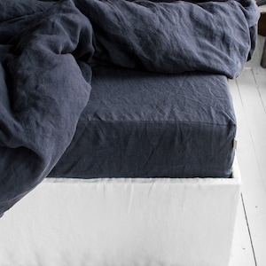 Op de afbeelding: Een donkerblauwe linnen bedrok met een witte linnen boxspring. De bedrok is gemaakt van een zachte, natuurlijke stof en heeft een eenvoudig, elegant ontwerp.