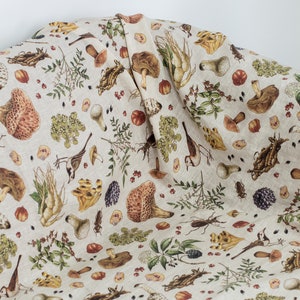 May include: A beige fabric with a repeating pattern of mushrooms, birds, and leaves. The fabric has a subtle linen texture.