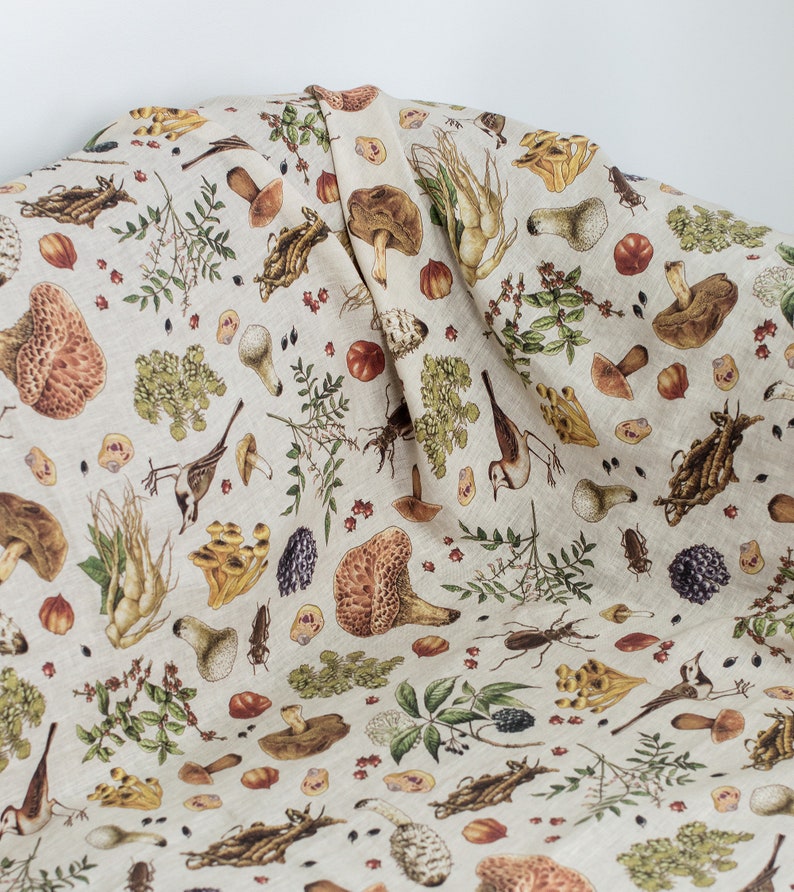 May include: A beige fabric with a repeating pattern of mushrooms, birds, and leaves. The fabric has a subtle linen texture.