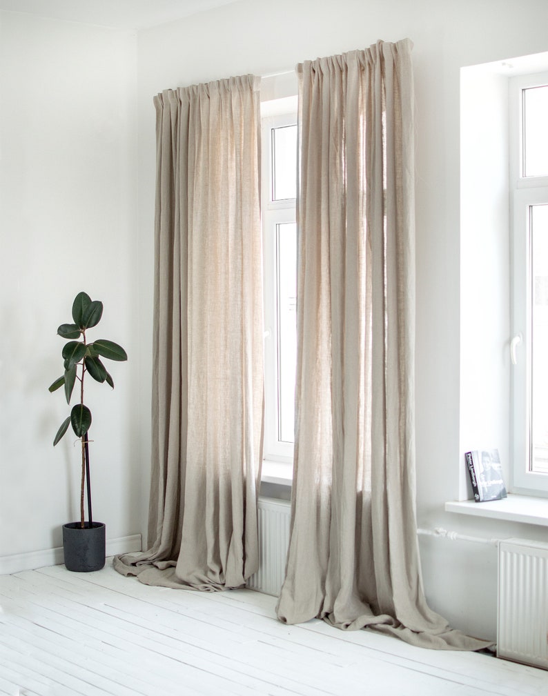 May include: Two pairs of beige linen curtains hanging in a window. The curtains are gathered at the top and hang to the floor. The windows are white and have white trim.