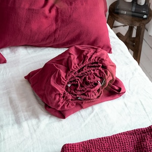 May include: A folded burgundy fitted sheet with a white background. A burgundy waffle weave throw blanket is in the foreground.