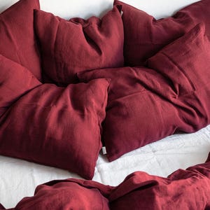 Peut inclure: Un ensemble de linge de lit en lin rouge foncé composé de taies d'oreiller et d'une housse de couette. Le tissu a un aspect légèrement texturé.