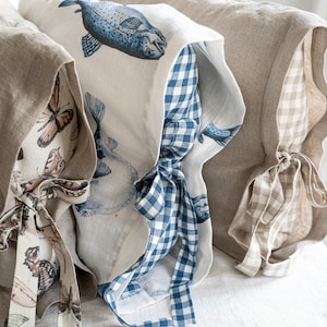 May include: Close-up of three decorative pillows with unique designs. One pillow features a blue fish print, another showcases a butterfly pattern, and the third has a neutral gingham pattern. Each pillow has a matching fabric tie.